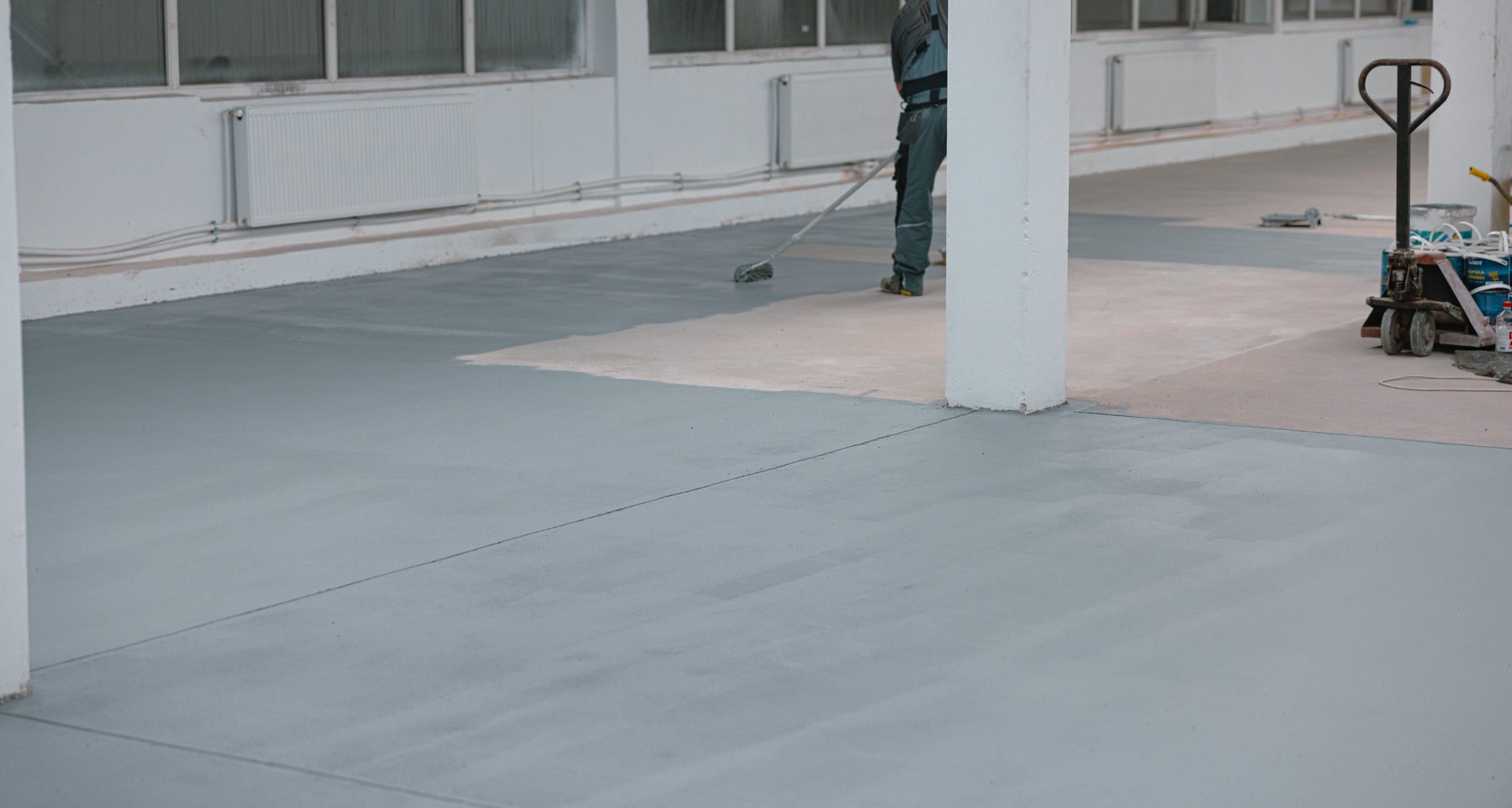 Worker paints the concrete floor with liquid gray paint